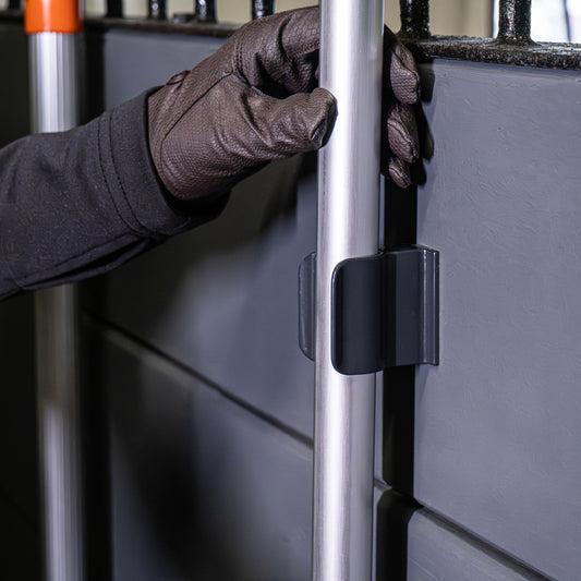 A gloved hand adjusts a metal pole with VPLAST round handles, secured by a Forever Fork HOLD IT Tool Holder mounted on a gray wall panel.